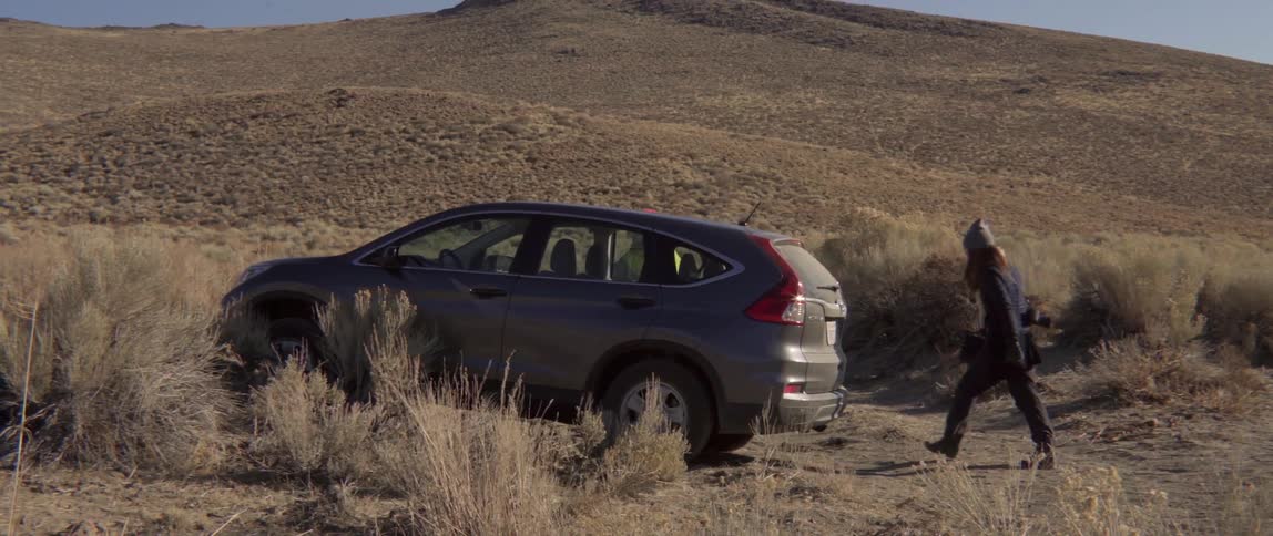 People running toward their parked vehicle near rolling hills with energetic motion.