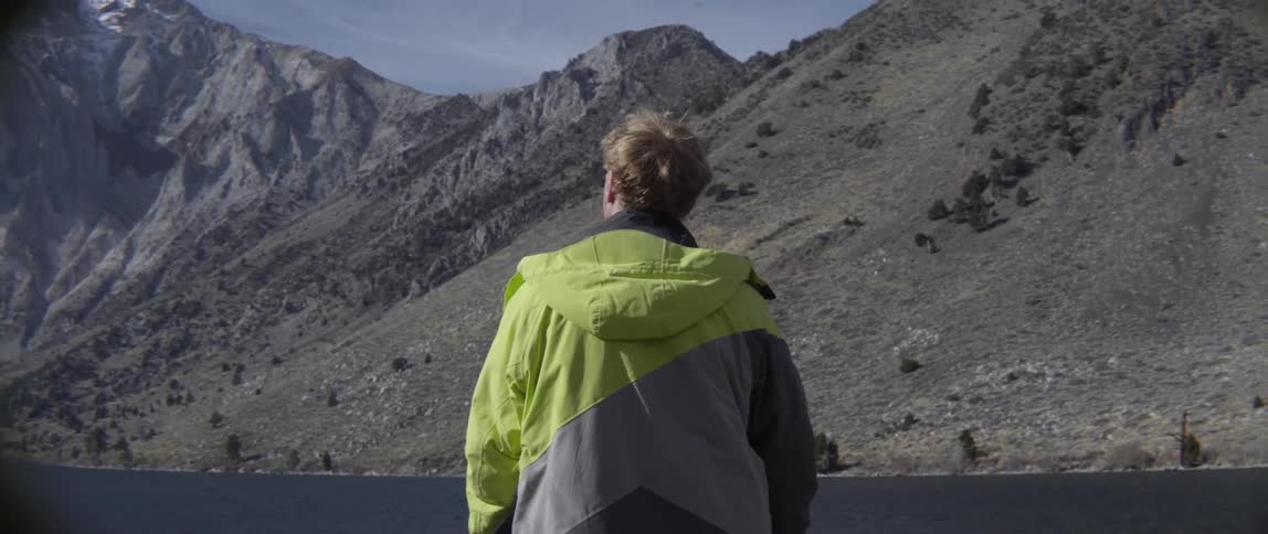 Man Standing and Overlooking Calm Water With Mountain Range in the Distance in Quiet Reflection.