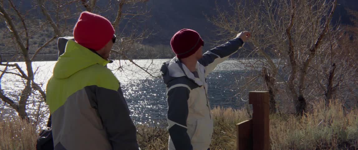 Man Pointing Out Over the Water While Two People Watch in Quiet Wonder Together.