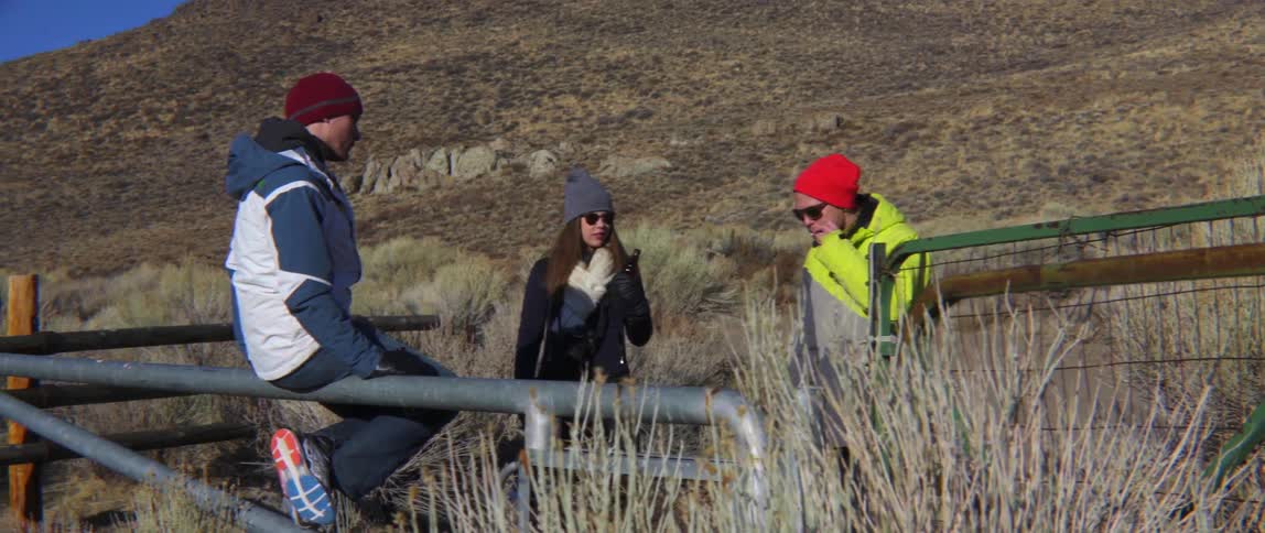 Three friends drink and talk while near a fence in the outdoors