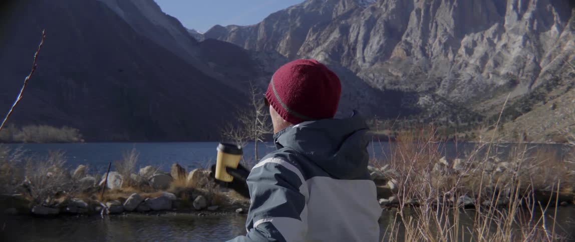 A man drinks as he looks over the water to a mountain range
