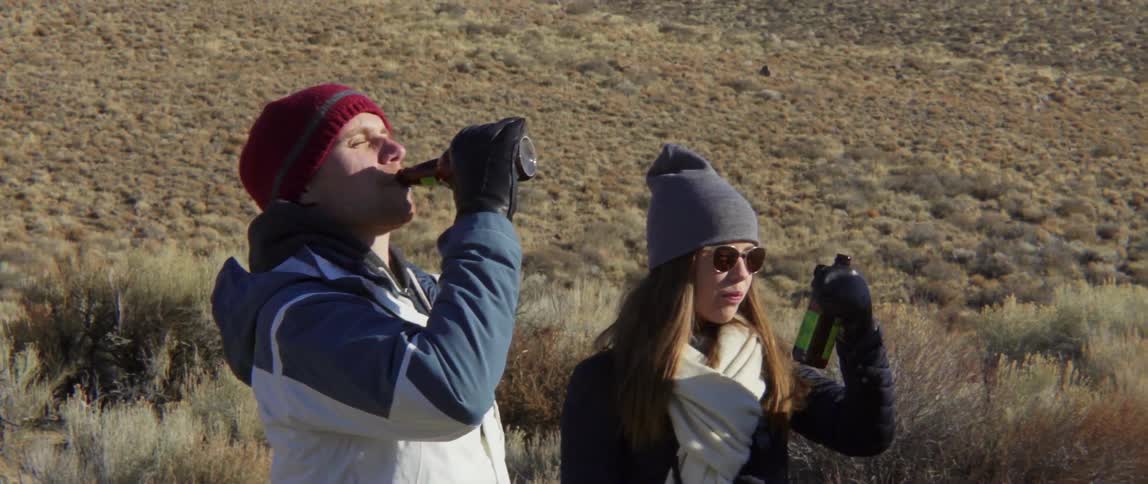 Man and Woman Drinking Beer Together While Another Man Talks in a Warm Outdoor Moment.