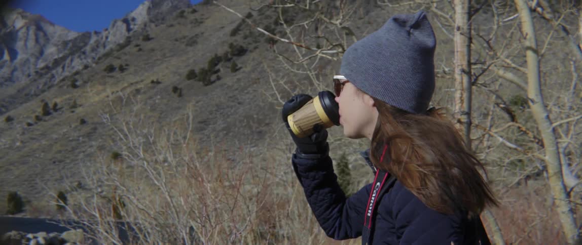 Woman drinking from a cup near tall hill with calm reflective mood.