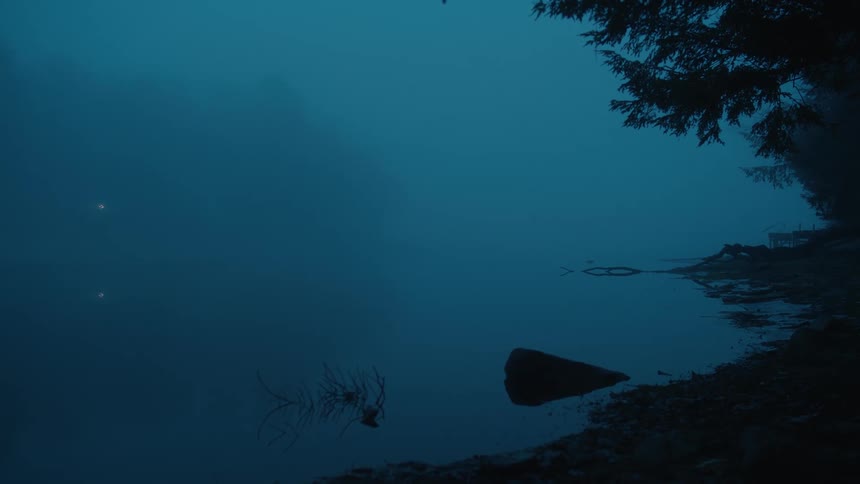 Mist over the forest near the calm surface of a lake at evening
