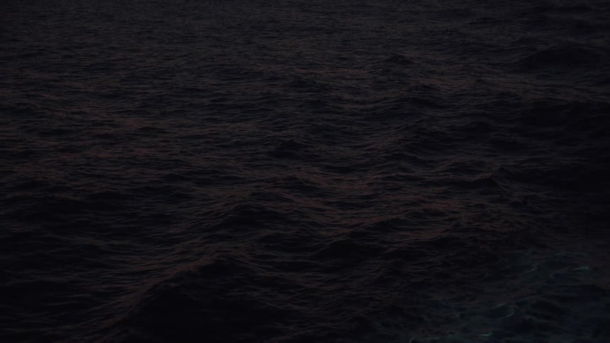 Waves roll across ocean surface at night creating foam