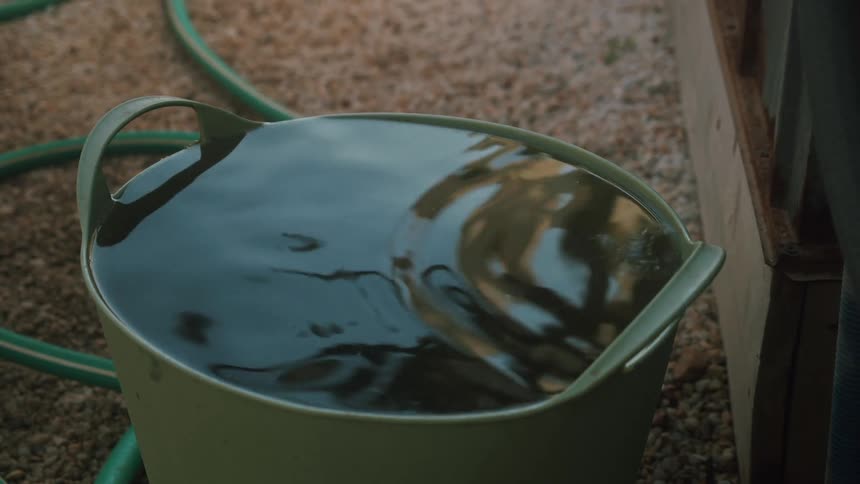 Water rippling in a pail next to a garden hose