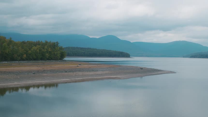 Water reflects clouds with forest and misty mountains in the background