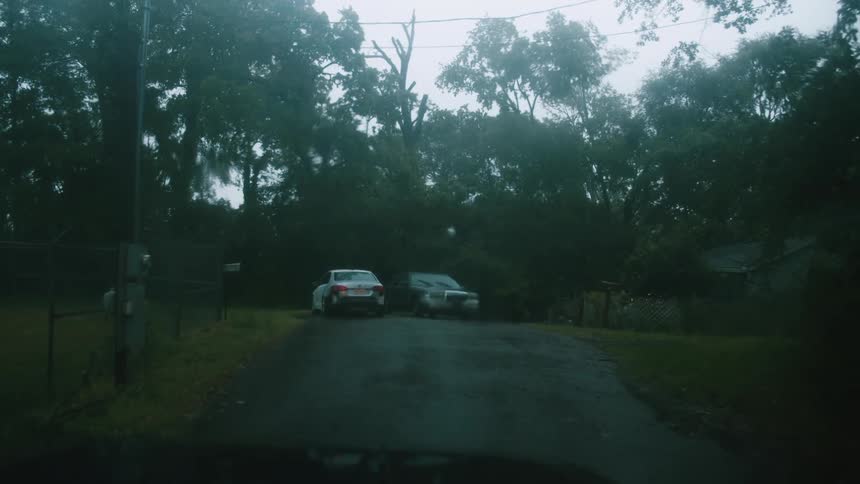 Rain drops fall blurring and distorting the image of cars parked near a remote home