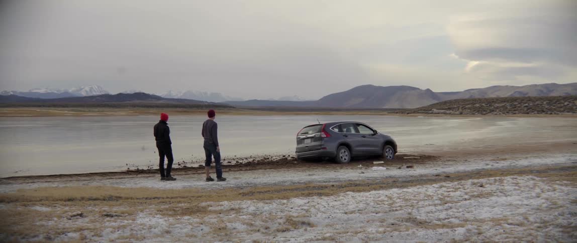 Two People Stand Behind Their Crashed Car in Quiet Shock Unsure What to Do.