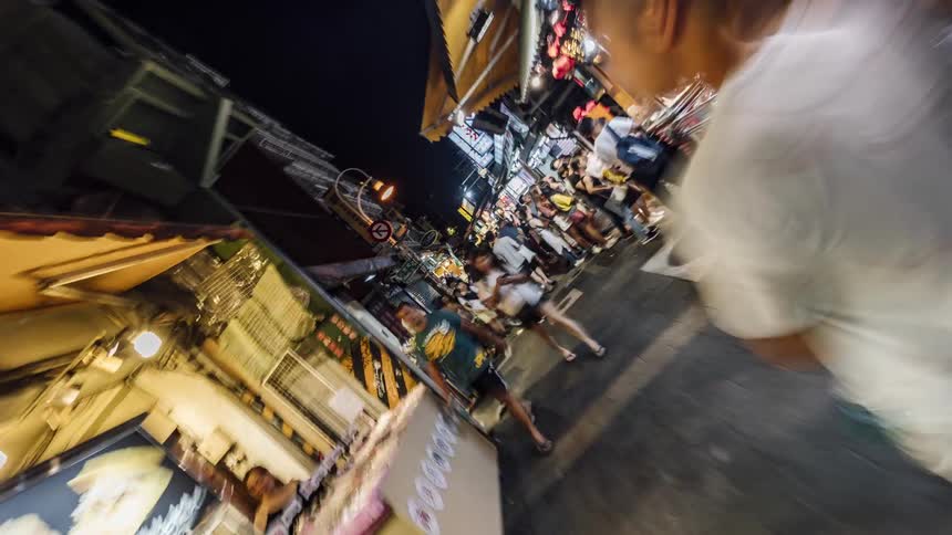 Spinning time lapse footage of people walking on a street market in the city at night