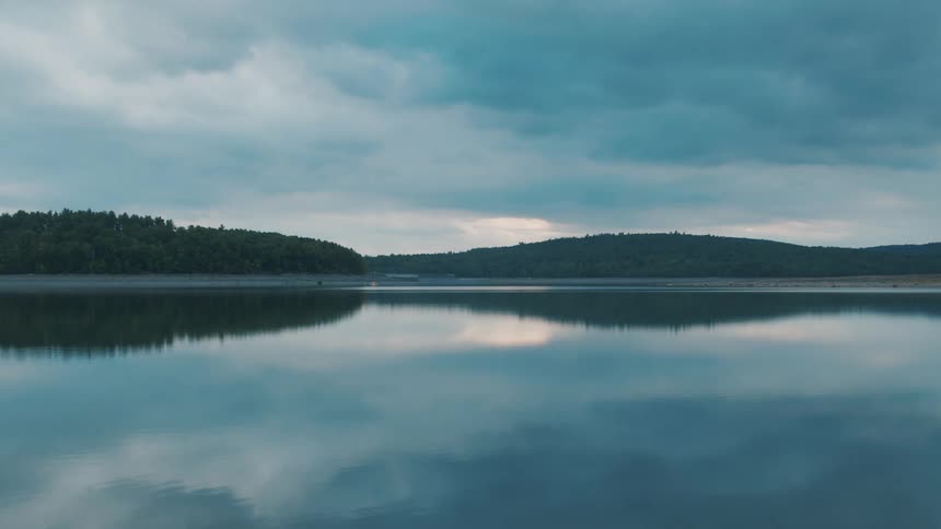 Hills trees sky and clouds all reflected on a shimmering rippling lake surface