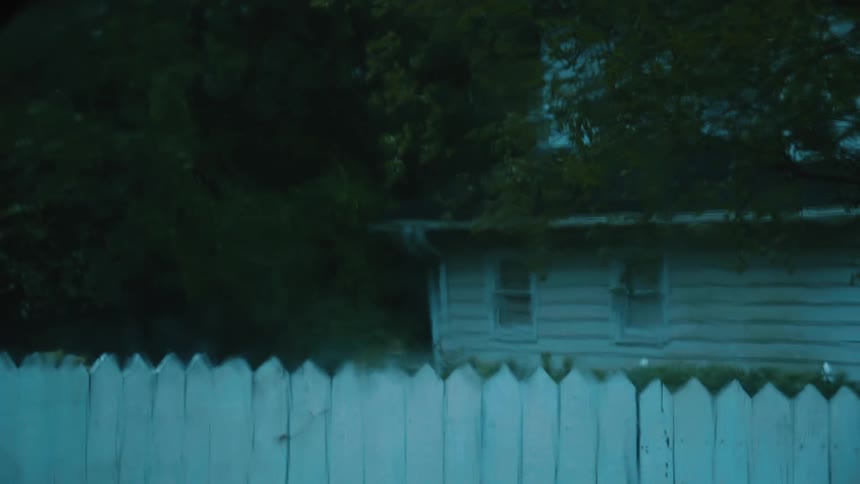 Rain drips down the window glass near a fence and house