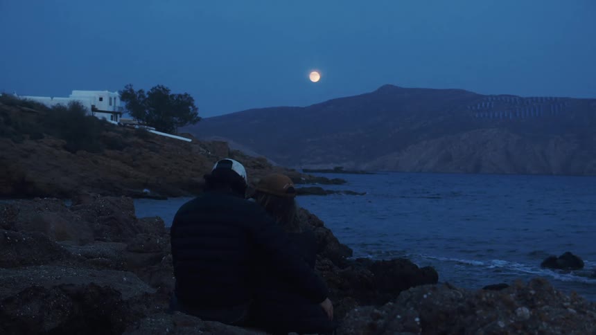 A man and woman cuddling on a lakefront with the moon glowing in the sky