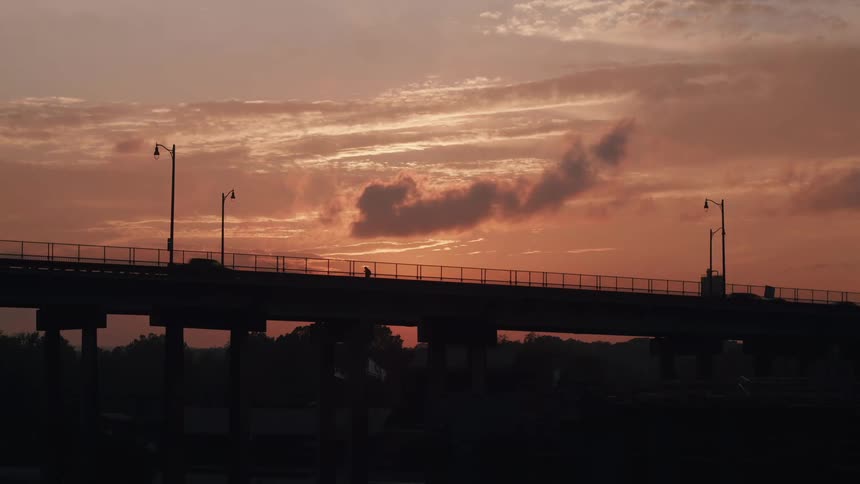 Vehicles and a person walk across the bridge at sunset