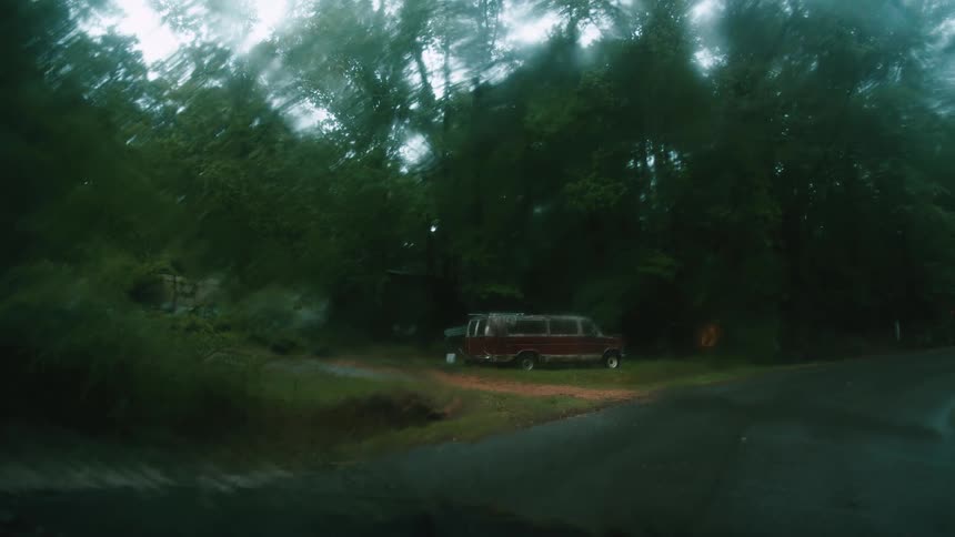 Water droplets sliding on the windshield of a car parked near a car in a rural area under the rain