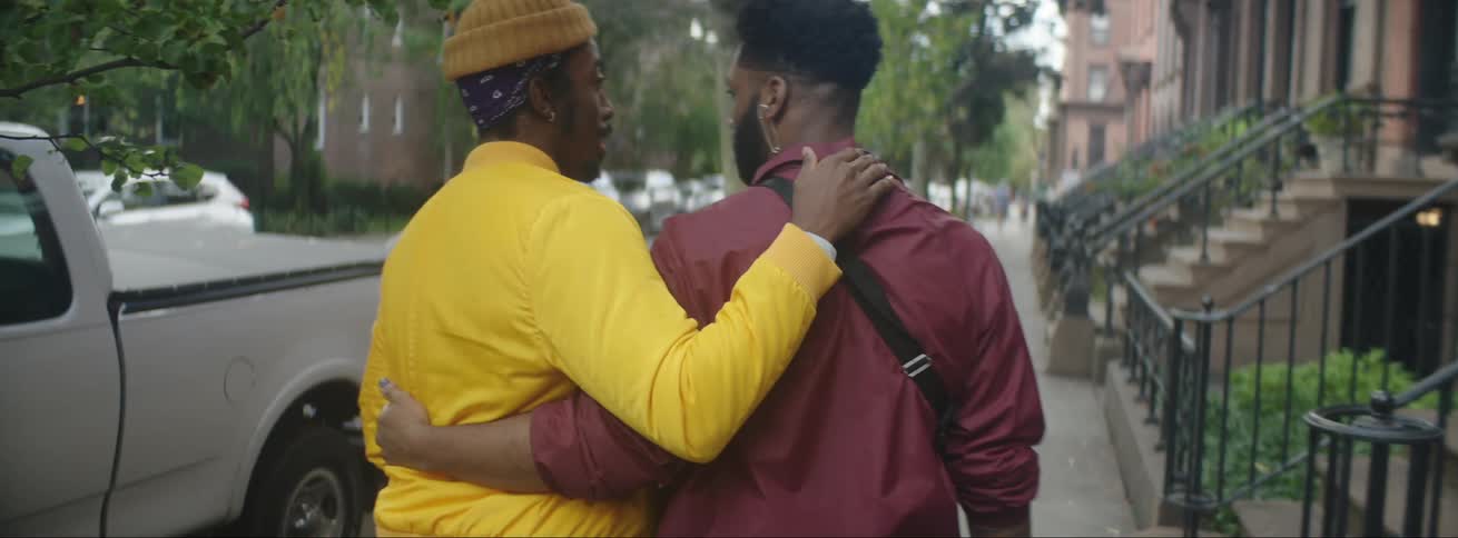 Two men walk down the street with their arms around each other