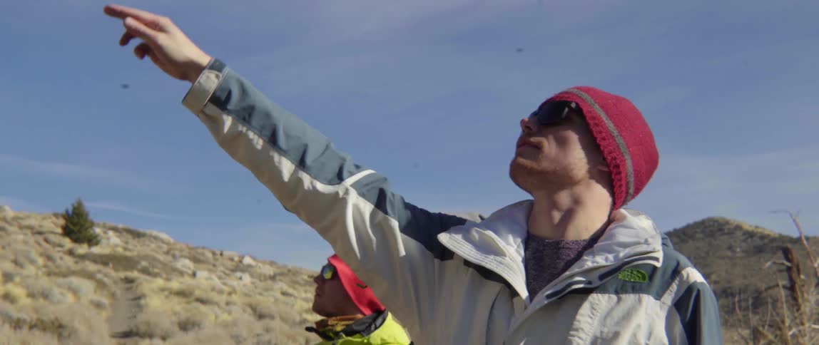 Man Points Up at the Sky While Others Watch With Curious Smiles and Connection.