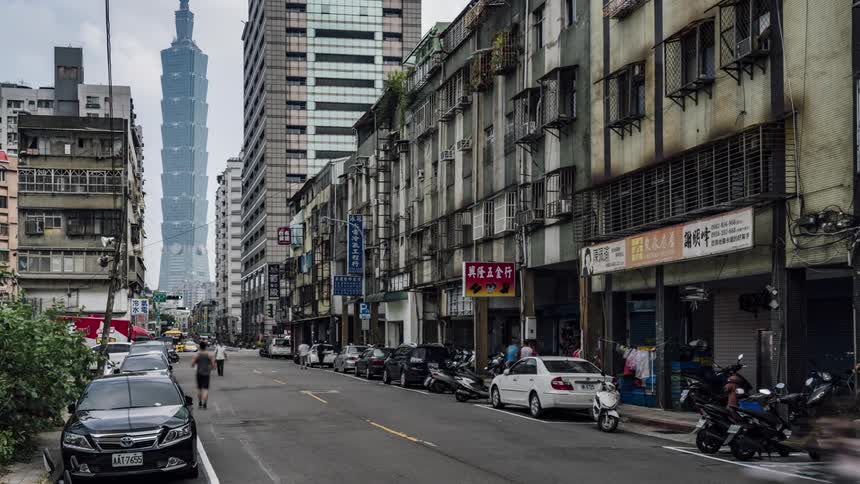People in vehicles and on bikes pass through a busy city neighborhood