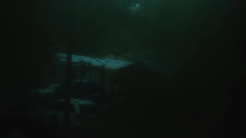 Water droplets sliding on a window looking at a car parked near a house in a rural area under heavy fog and rain
