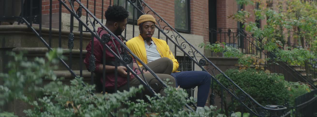 Two friends wearing colorful outfits talking while sitting on the stairs of a building