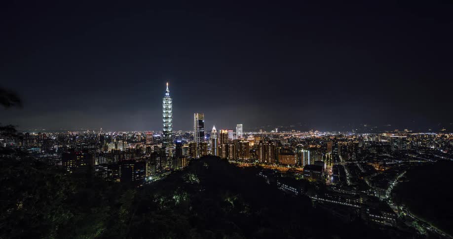 Clouds move across brightly lit downtown towers near tall spire topped building