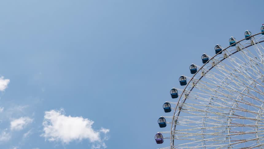 Timelapse footage of a ferris wheel spinning in front of white clouds on the blue sky