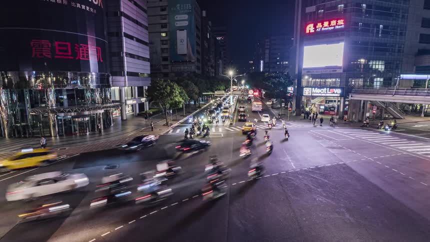 People and traffic move through a busy city intersection while digital billboards and signs flash at night
