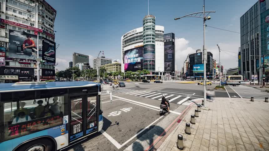 Pedestrians and traffic moves through intersection near buildings showing images on their side