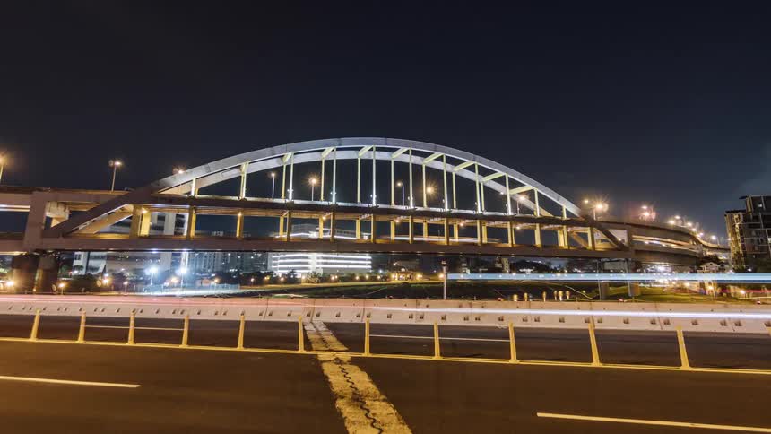 A timelapse of vehicles driving in front of a large city bridge at night
