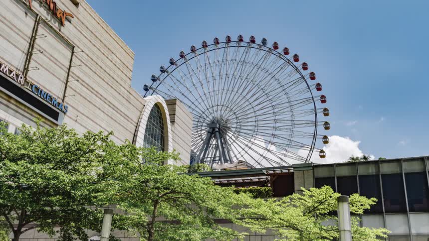 Ferris wheel rotates near movie cinema under a cloudy sky
