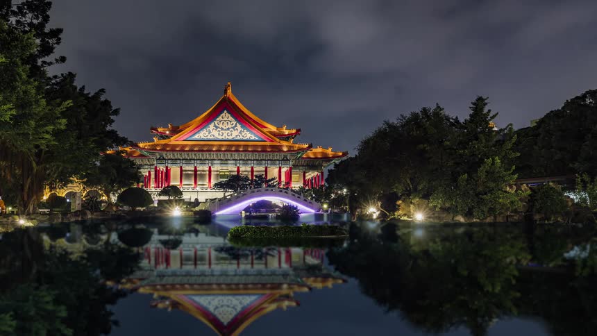 Time lapse of boats driving under a bridge with bright colorful lights in front of a pagoda at night