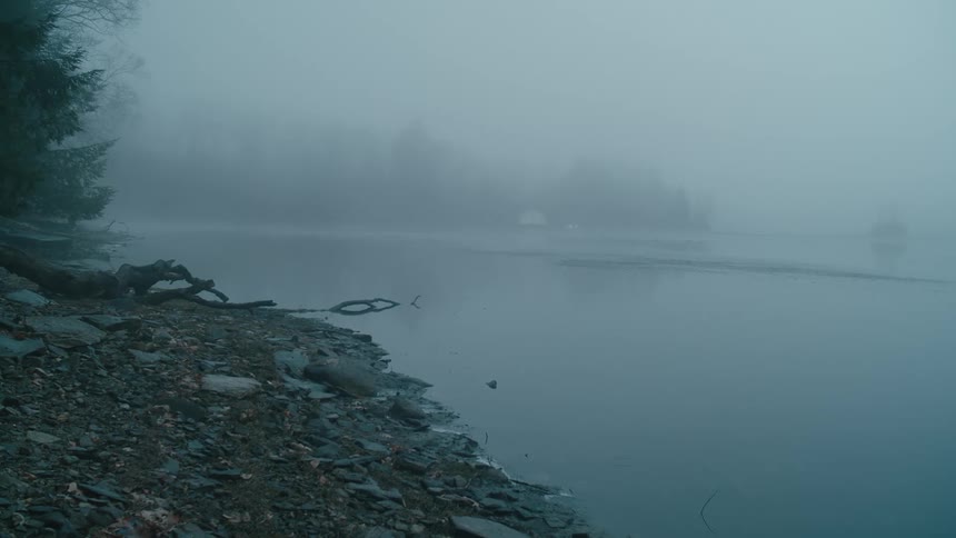 Snow is lightly falling on the beach of a lake