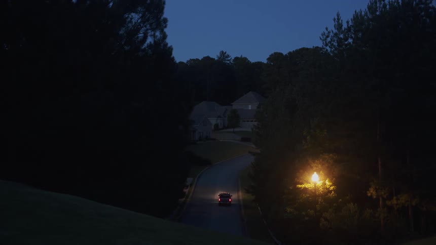 A vehicle drives up a driveway to a home in a rural area at night