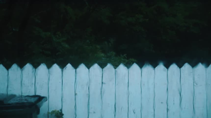 The rain is hitting the window and white fence outside