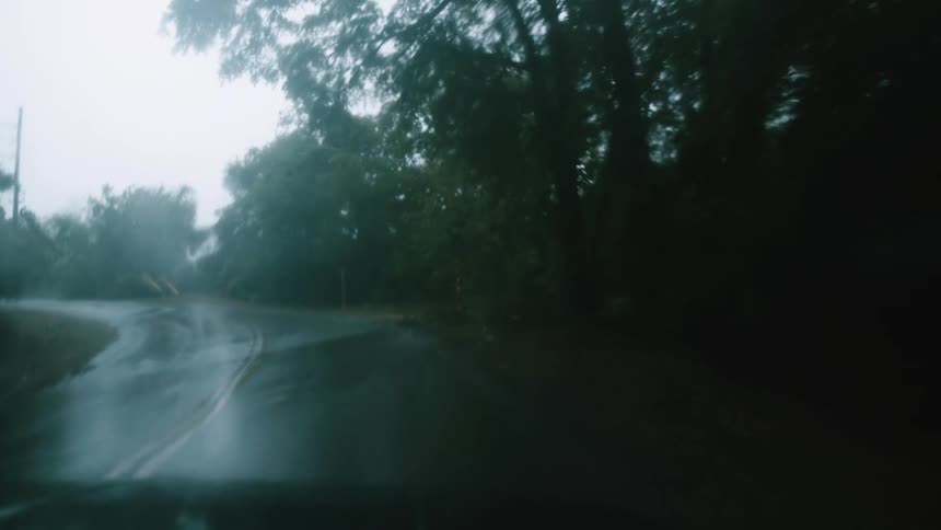 View through the windshield traveling on a road through the woods in the rain