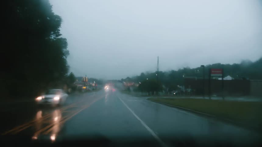 A car drives past businesses while it rains