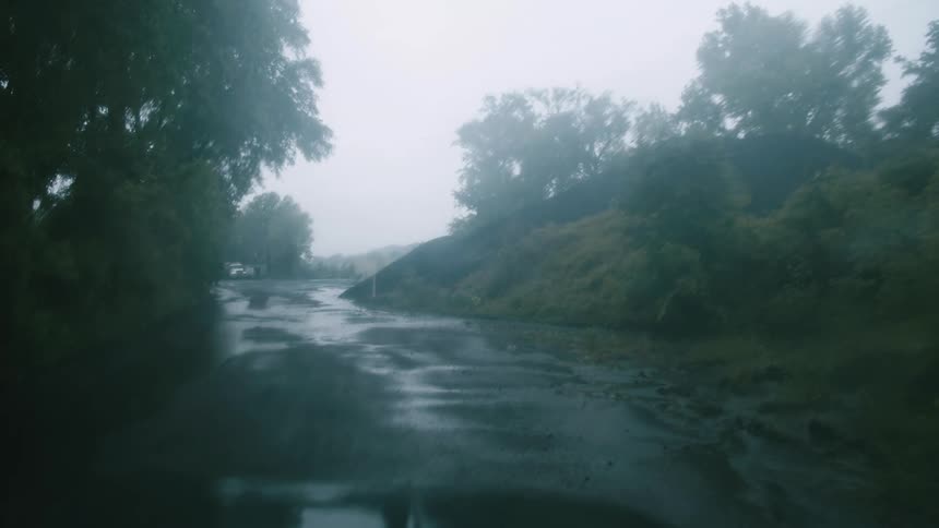 Windshield wipers move on a vehicles windshield as it sits on a road with rain falling