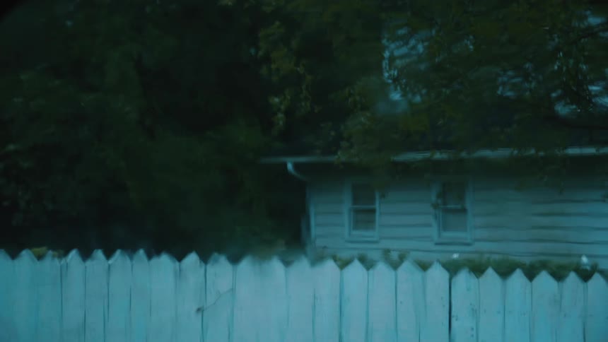 Rain water dripping down a window looking at a rural home behind a white fence