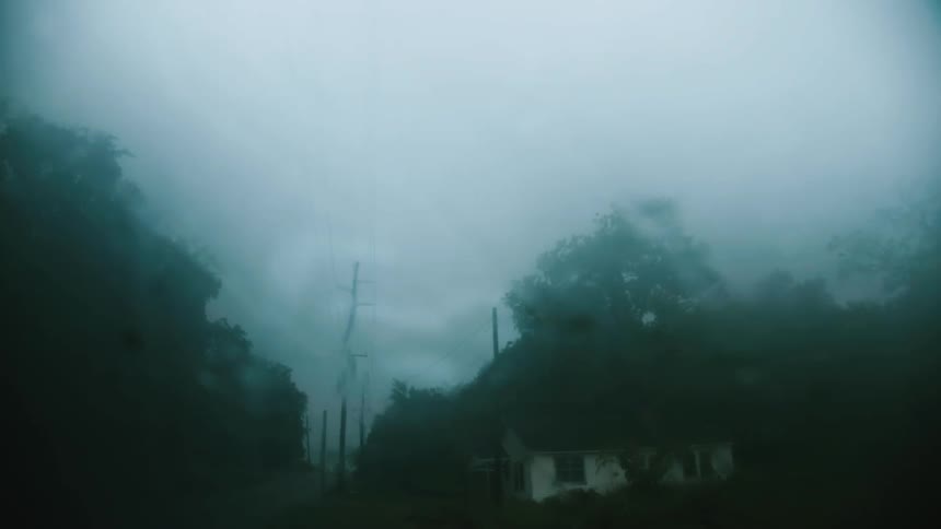 Water droplets sliding on the windshield of a car parked near a house in a rural area under the rain