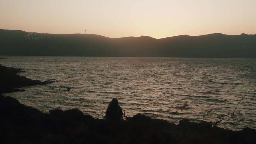 The silhouette of a person sitting on shore looking out at the water