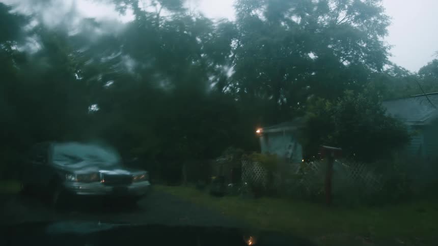 A small house and parked car during a summer rainstorm