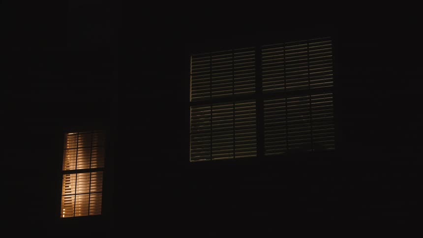 Static shot of light coming out of a house window at night