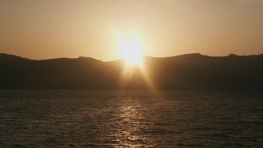 The sun shines brightly over mountains as it reflects on the water as it ripples