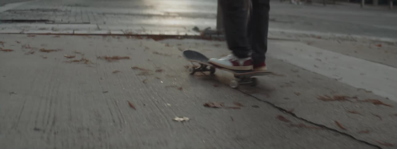 Skateboarder stops and picks up his board as he waits for traffic to pass at a city intersection