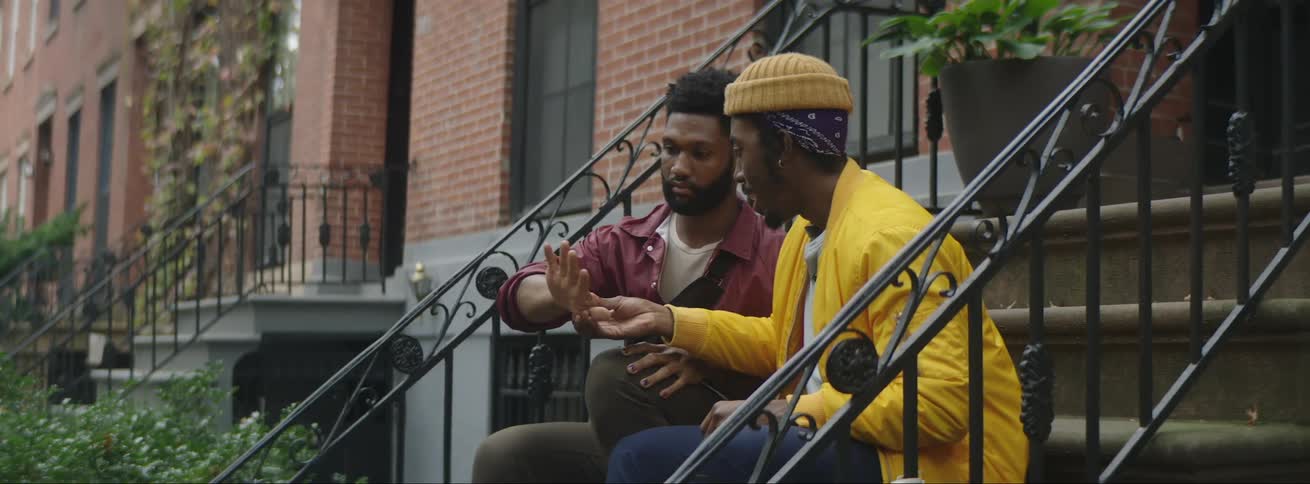 A man examines his friends hands as they sit on the stoop of a brownstone