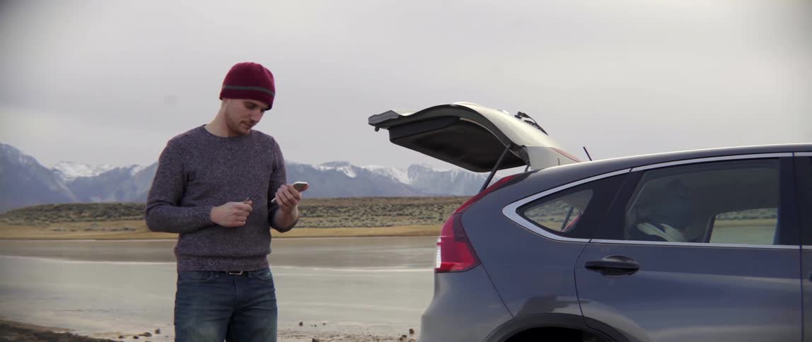 Man Standing by Open Car Trunk Using His Phone With Quiet Focus After Travel.