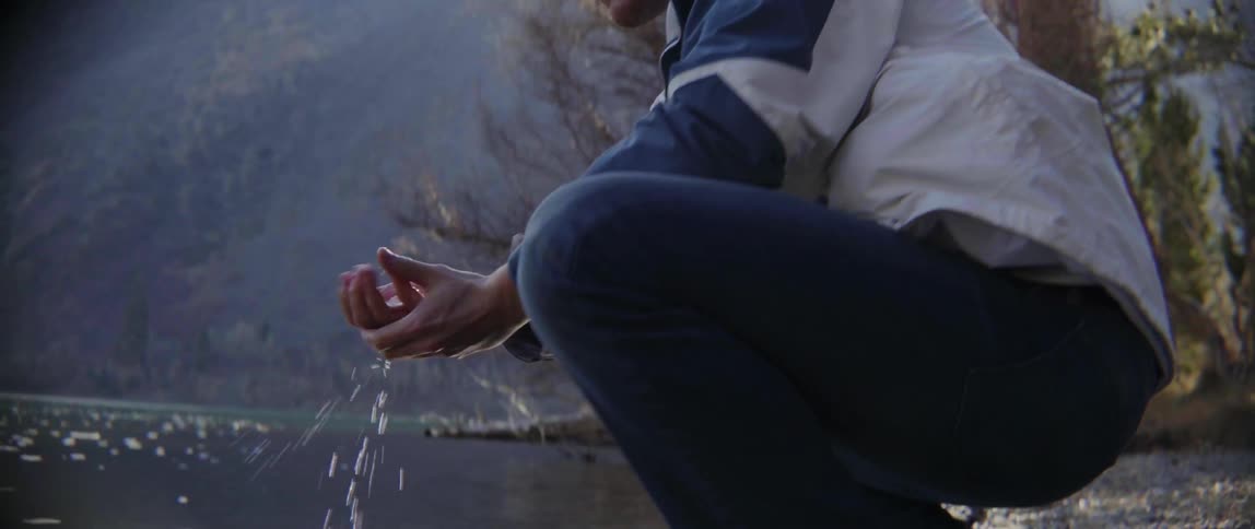 A man wipes his hands with water as he is crouched by a pond