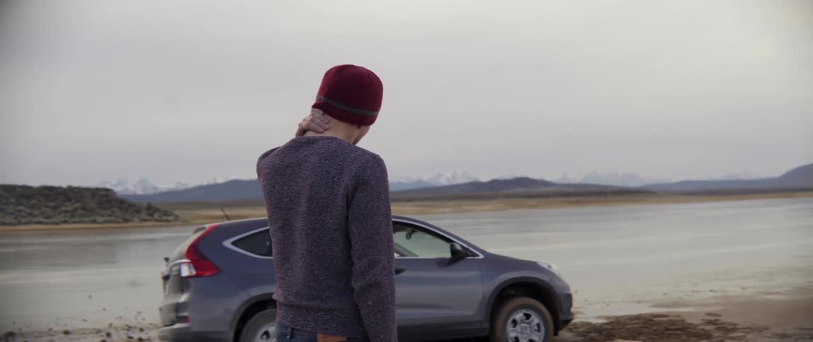 Person rubbing his ear while looking to crashed car in total stress and confusion.