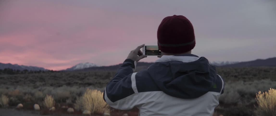 Man capturing the setting sun with his phone in warm golden light.