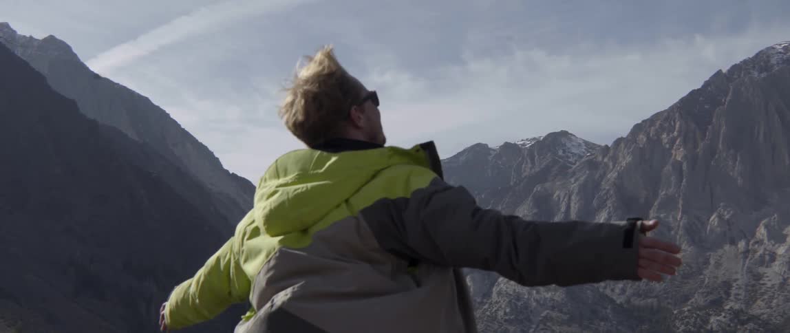 A man stands on a mountain range outstretching his arms